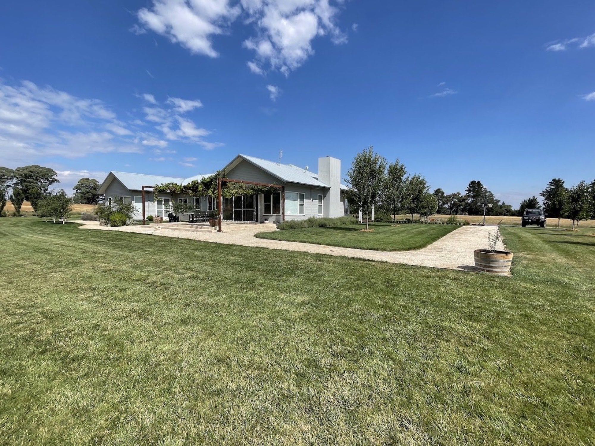 A wide cut lawn in front of a lowset home with a Colorbond roof under a big sky