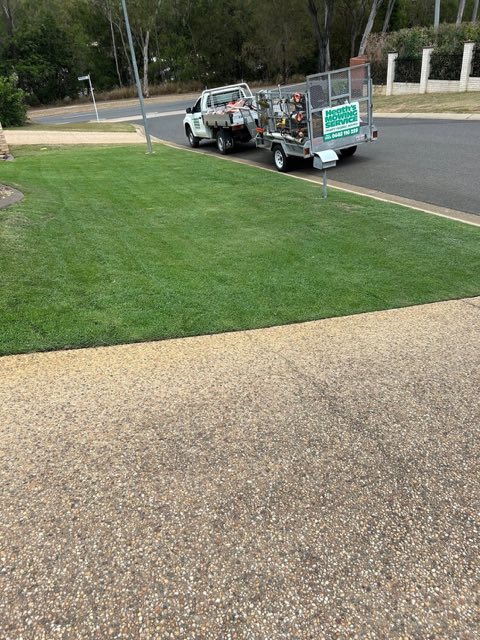A mown front lawn with a ute and trailer parked on the street behind it