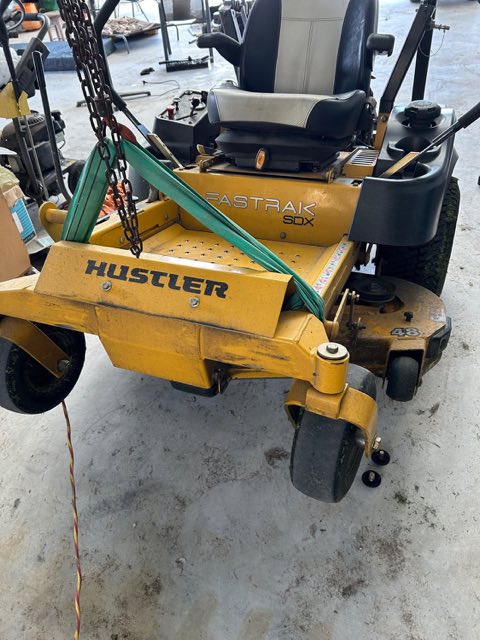 A yellow zero-turn ride-on mower slung on a lifting strap