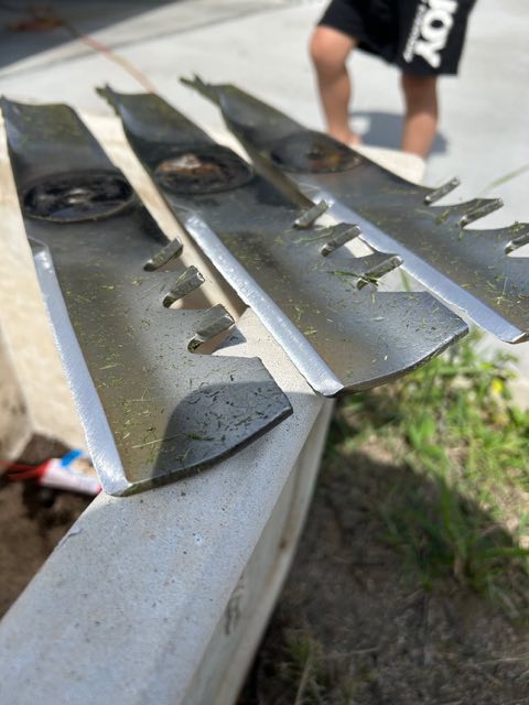 Three mower blades laid along the edge of a trailer