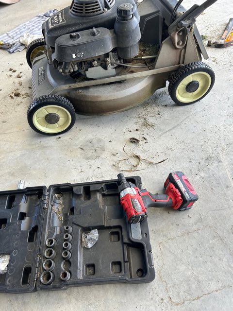 A push mower and an open tool case on a concrete driveway