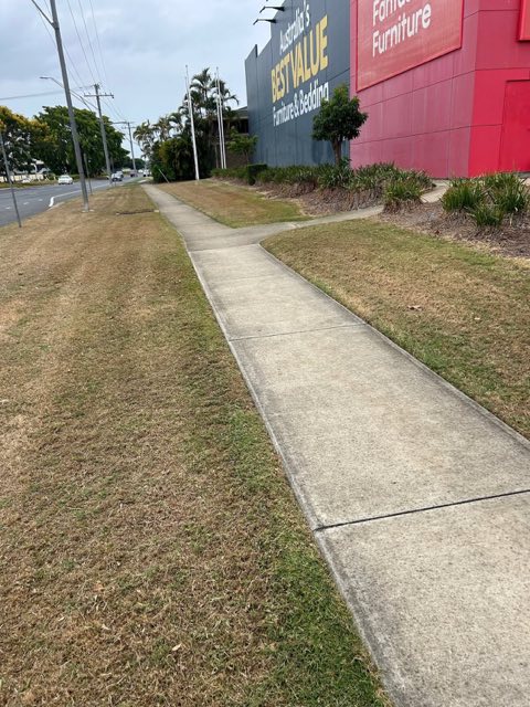 A cut nature strip running beside a footpath in front of a commercial building