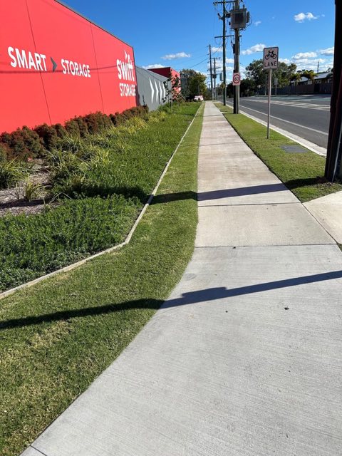 A mown verge and footpath running past a storage business on a main road