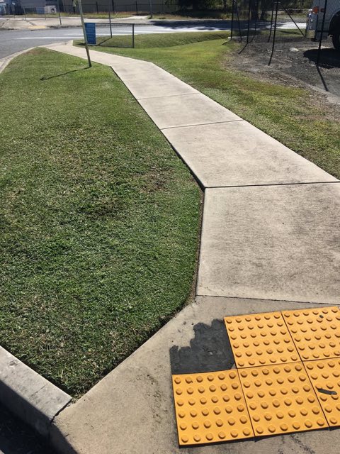 A footpath corner with tactile pavers beside freshly cut grass