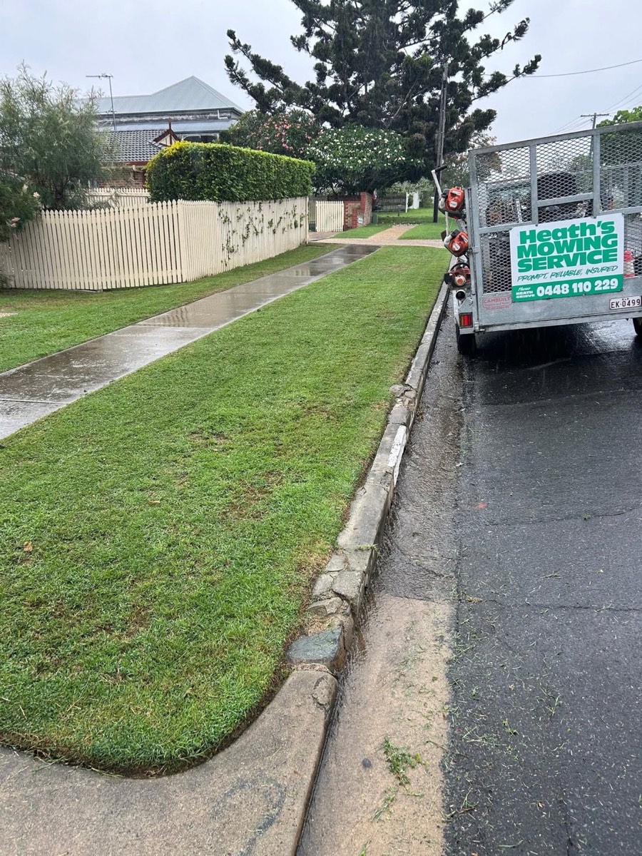 A trailer signwritten Heath's Mowing Service parked at the kerb beside a cut verge